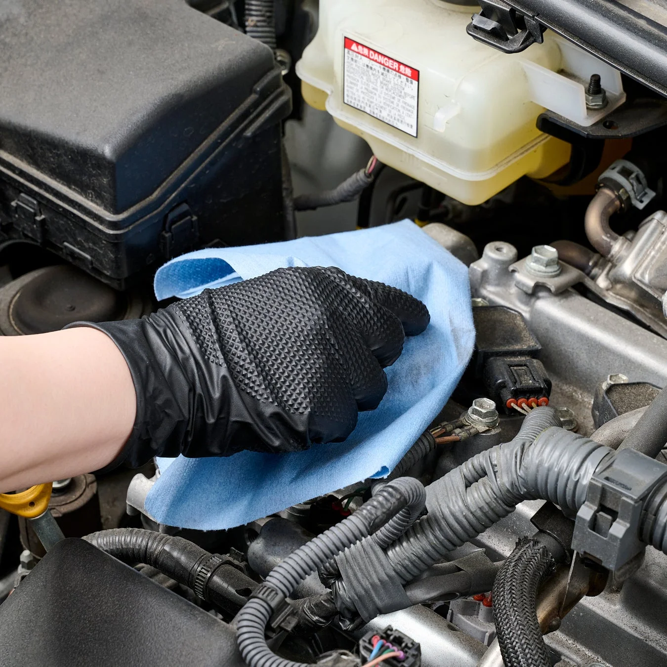 手袋をはめた手が青い布で車のエンジンルームを拭いています