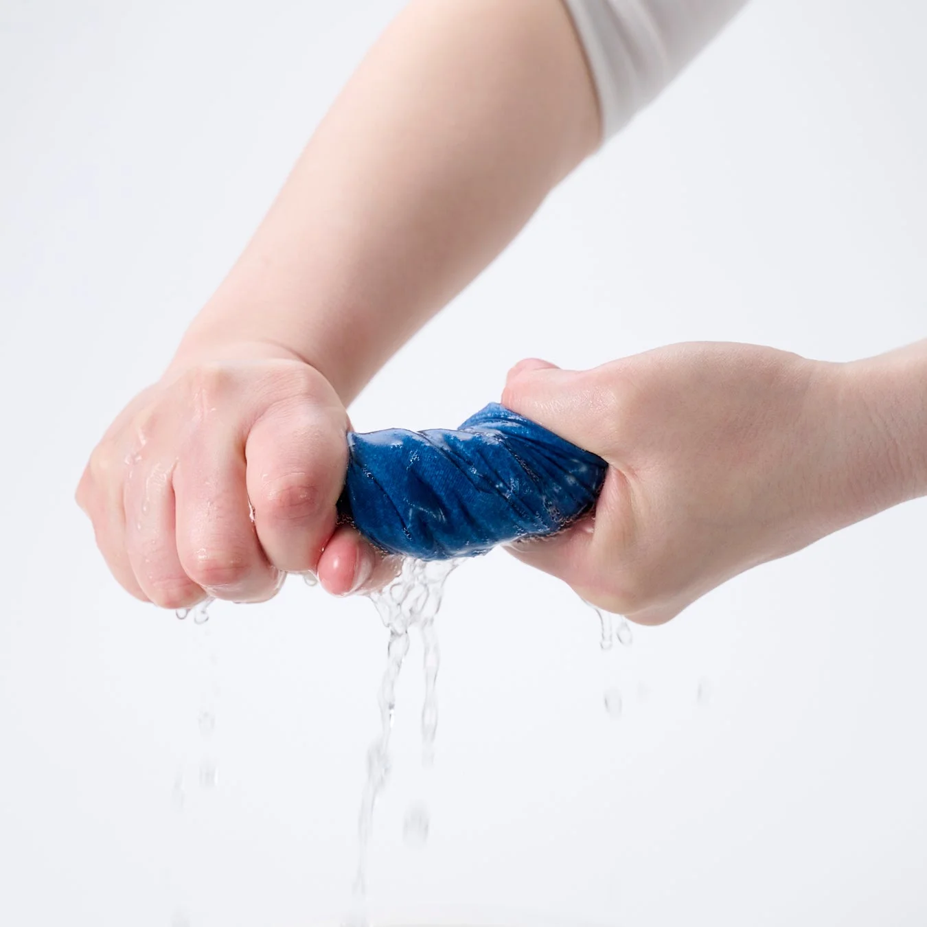 両手で青い布を強く絞っており、水が勢いよく滴り落ちている瞬間